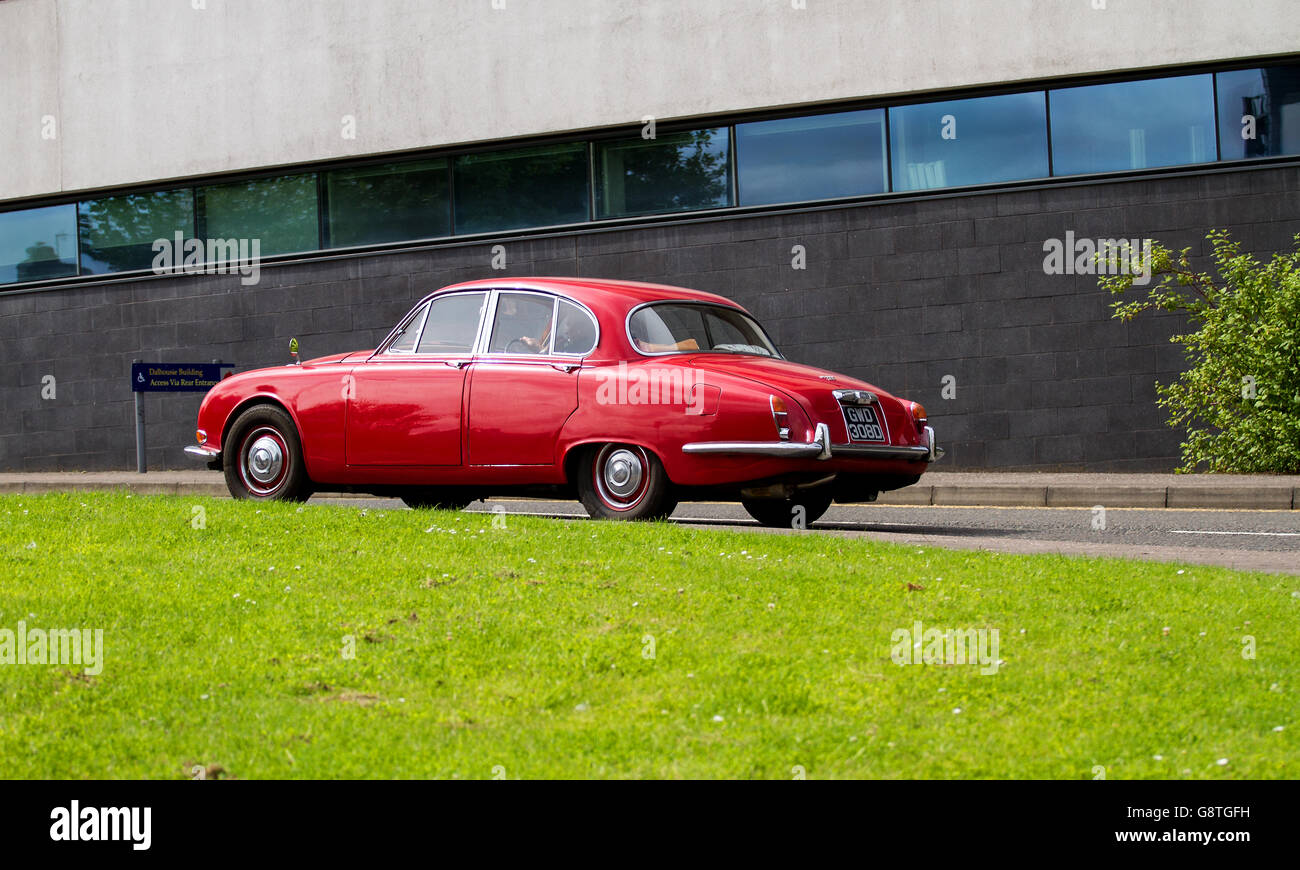 A red vintage 1960`s Jaguar 420 saloon car traveling past the Abertay University building in Dundee, UK Stock Photo